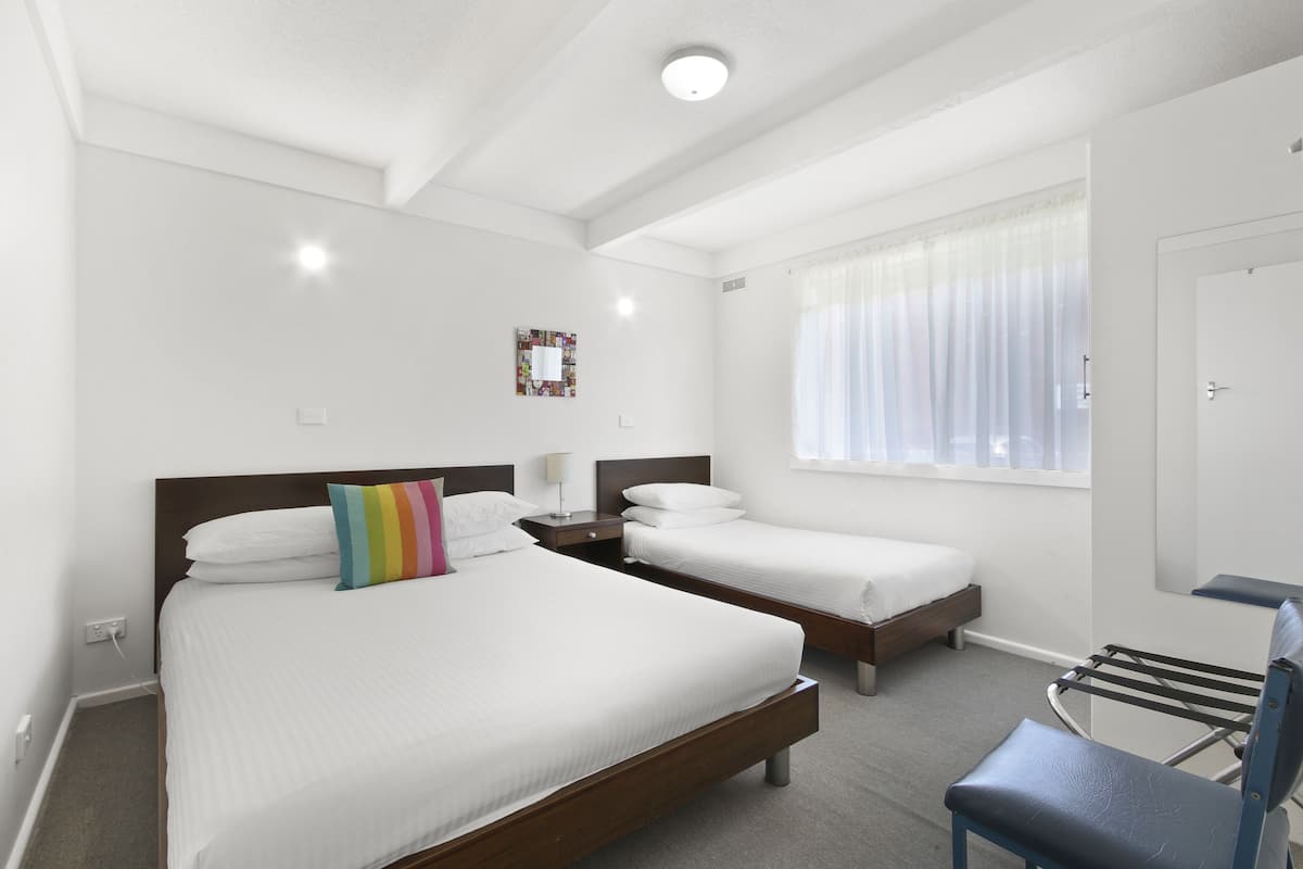 A hotel room with two beds, a desk, a chair, and a window with curtains.