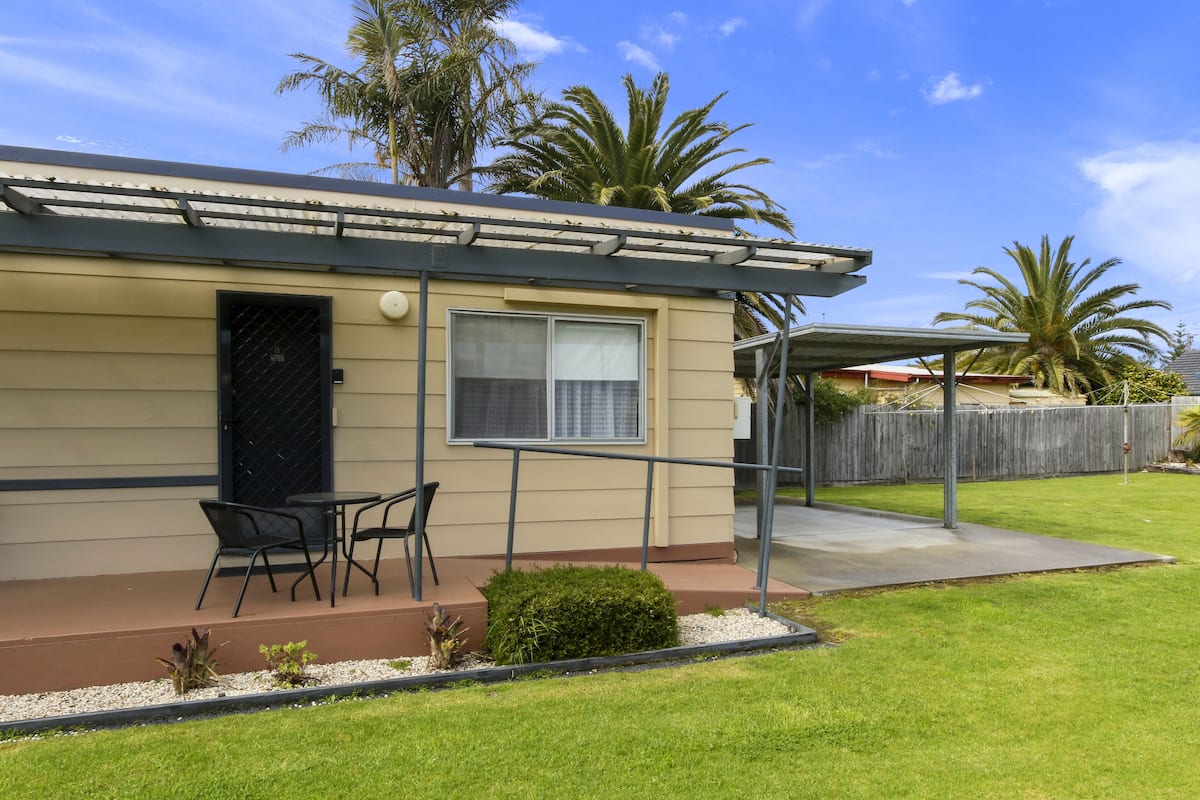 A single-story house with a covered patio, a small lawn, and a wooden fence.