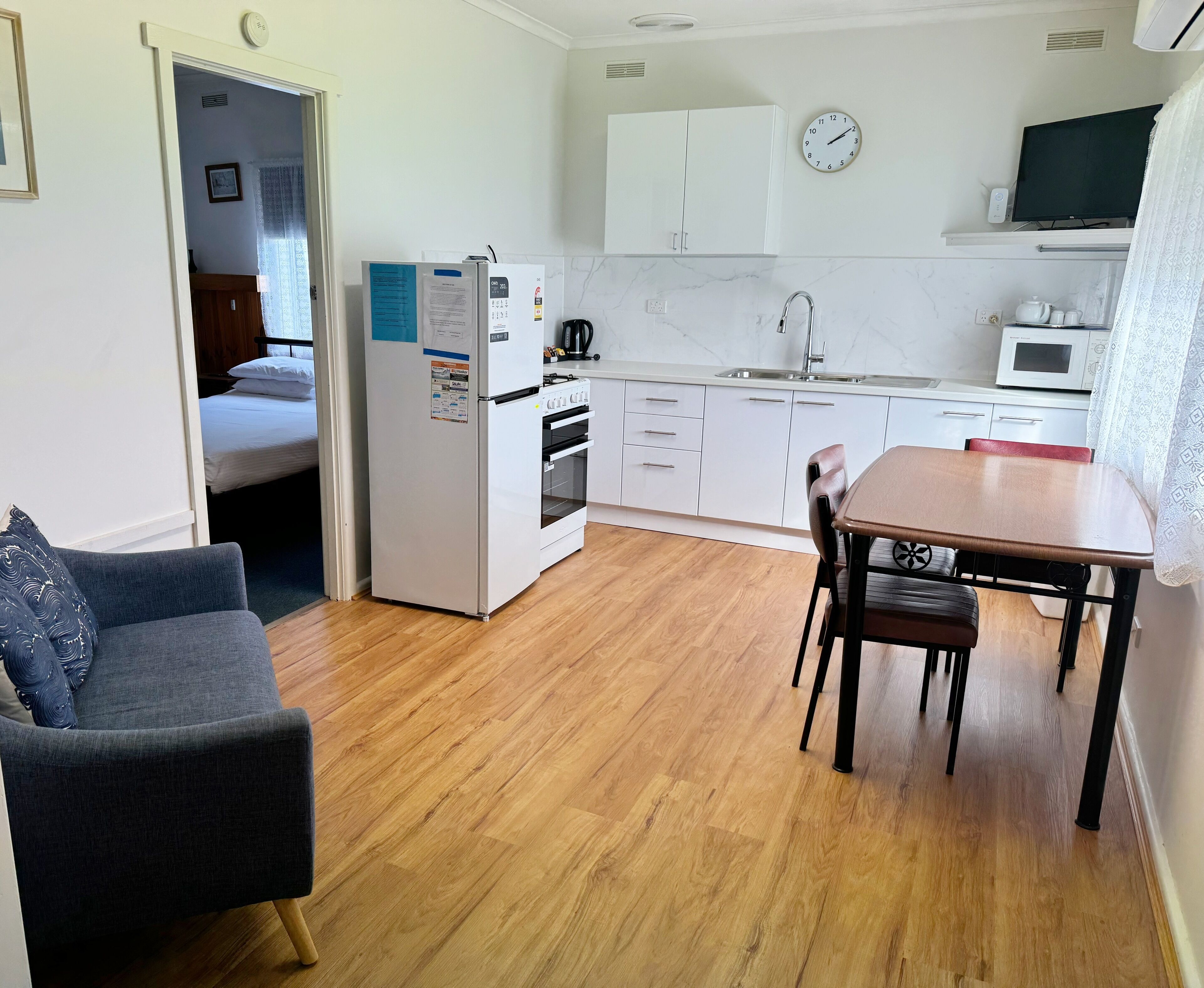 Een kleine keuken met een magnetron, oven en spoelbak. Er is een eettafel met stoelen en een bank in de woonkamer.