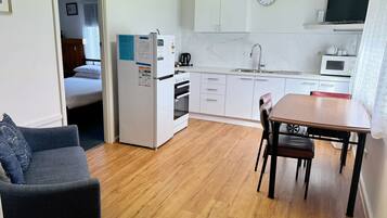 Een kleine keuken met een magnetron, oven en spoelbak. Er is een eettafel met stoelen en een bank in de woonkamer.