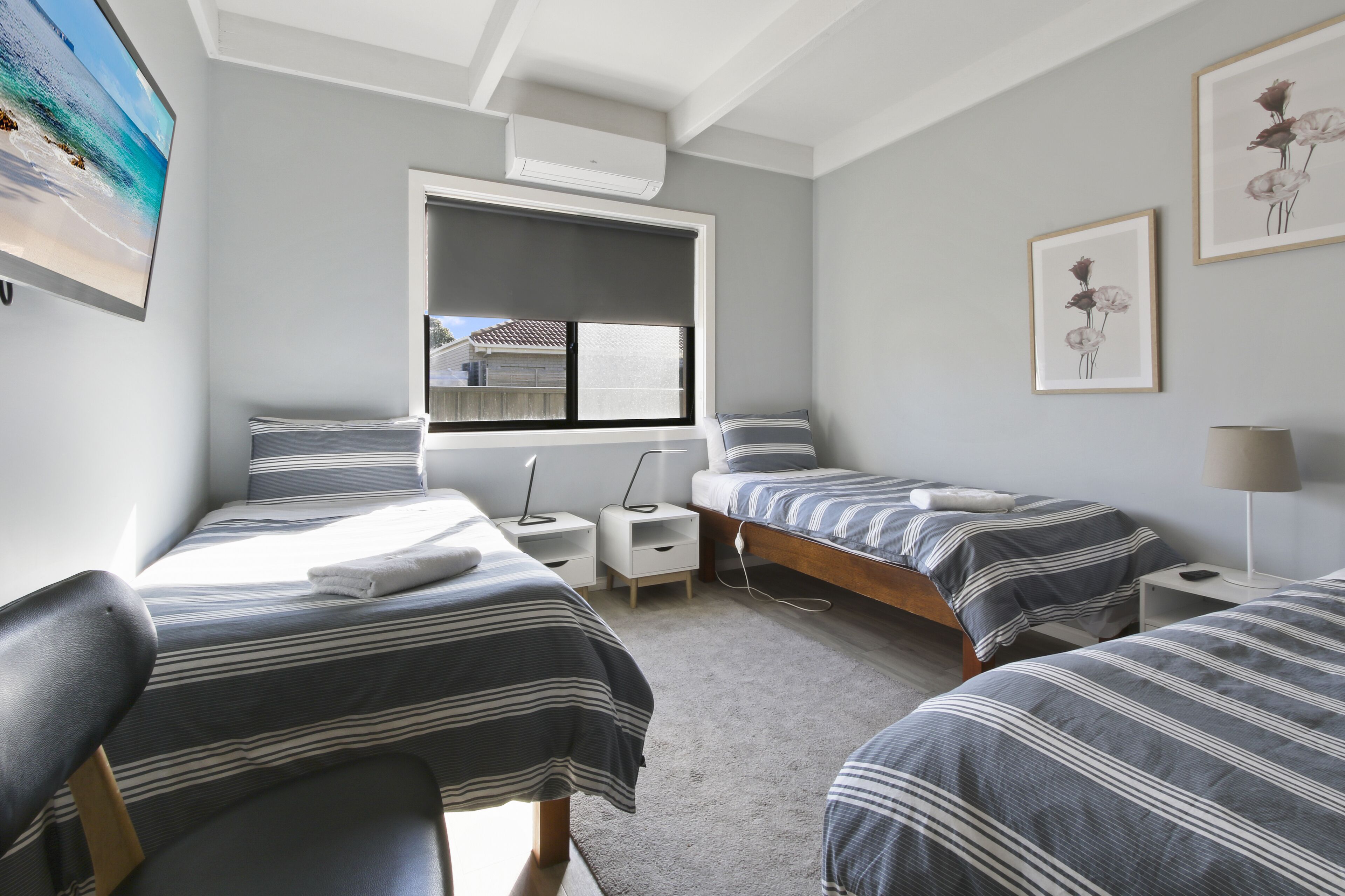 A bedroom with two beds, a window, a ceiling fan, and a painting on the wall.