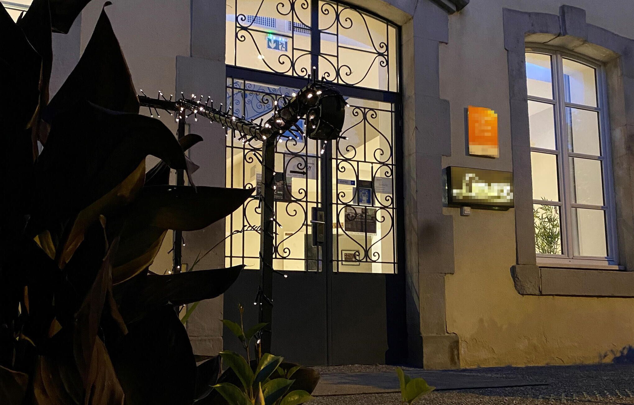 Entrada de un edificio con una reja de hierro forjado, un pequeño letrero y una ventana con vista a la calle.