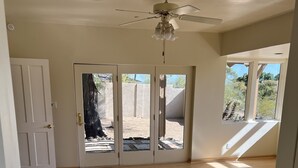 A spacious room with a wooden floor, a ceiling fan, and a sliding glass door leading to an outdoor area with a cactus.