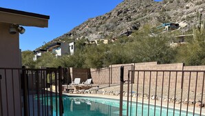 A swimming pool with a metal fence, surrounded by a gravel area and a building with a flat roof.