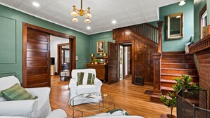 A spacious living room with a staircase, wooden floors, and a green accent wall.