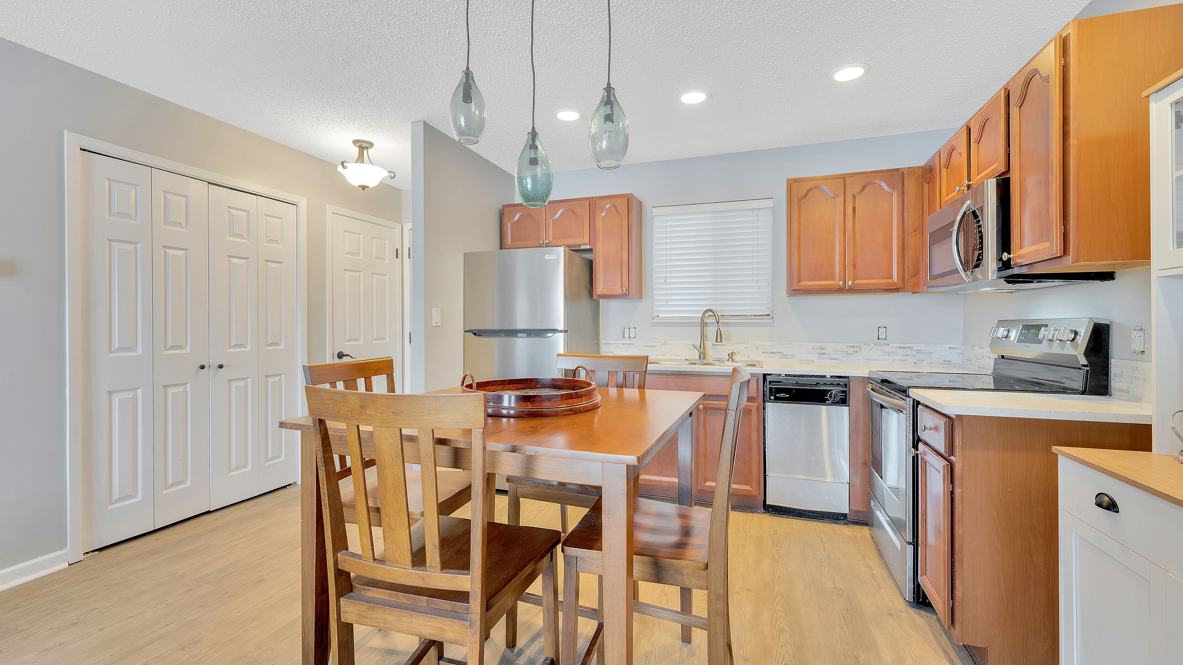 A modern kitchen with wooden cabinets, stainless steel appliances, and a dining area with wooden chairs and a table.