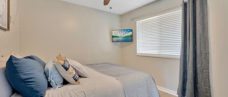 A bedroom with a bed, pillows, a ceiling fan, a window with blinds, and a framed picture on the wall.