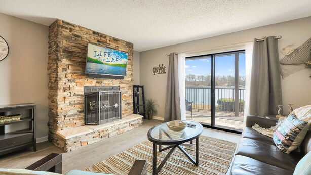 A living room with a stone fireplace, a large window with a view of the lake, a sofa, and a coffee table. - Gorgeous Updated Condo - Incredible view, no stairs from patio to lakefront/dock (Osage Beach)