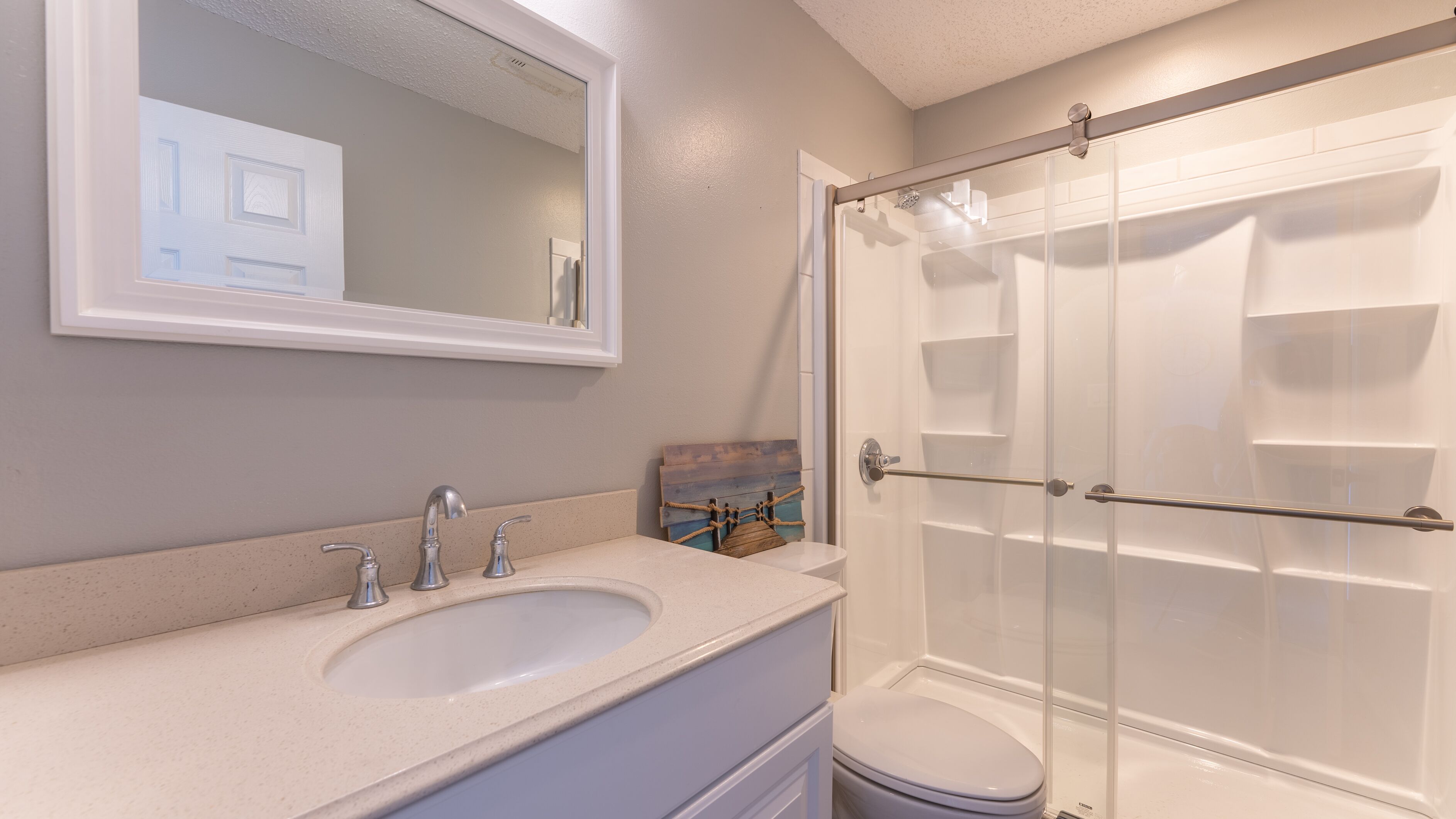 A bathroom with a double sink, a mirror, a shower enclosure, and a toilet.