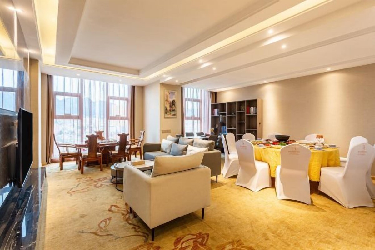 A spacious living room with a fireplace, a dining area with a yellow tablecloth, and a bookshelf.