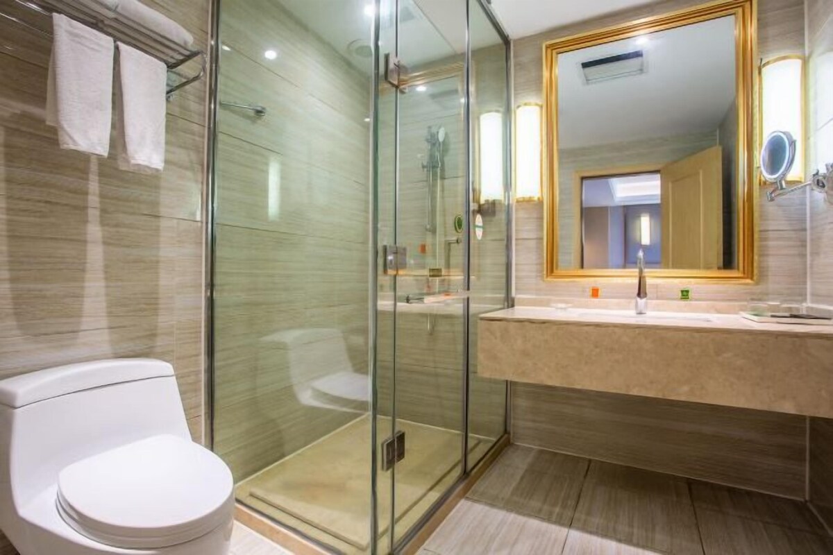 A modern bathroom with a glass-enclosed shower, a white toilet, and a beige vanity with a large mirror.