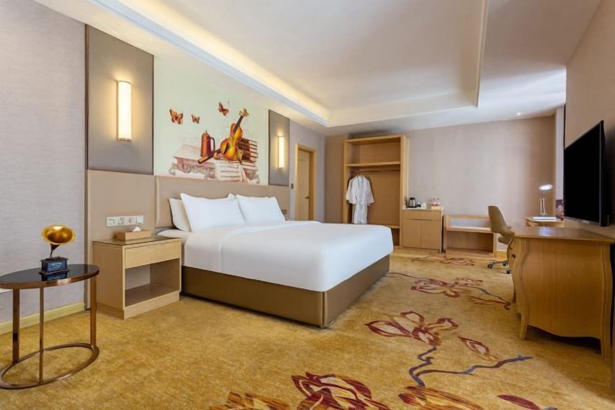 A hotel room with a bed, bedside table, lamp, desk, chair, and a television.