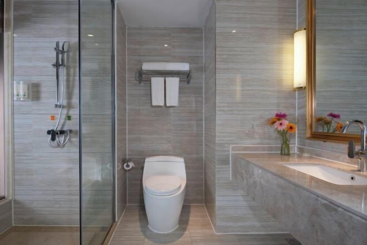 A modern bathroom with a glass shower enclosure, a toilet, and a sink with a mirror.