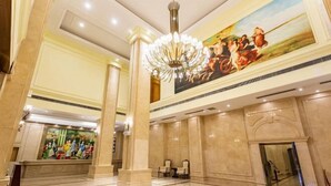 Un'ampia hall con soffitto alto, un grande lampadario e un affresco che raffigura una scena storica.