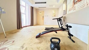 A hotel room with a carpeted floor, a standing desk, a treadmill, and a kettlebell. - Vienna International Hotel (Bijie Dafang Branch) (Bijie)
