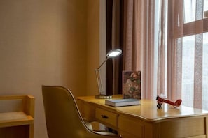 A hotel room with a wooden desk, a chair, a desk lamp, a book, a small airplane model, and a window with curtains. - Vienna International Hotel (Bijie Dafang Branch) (Bijie)