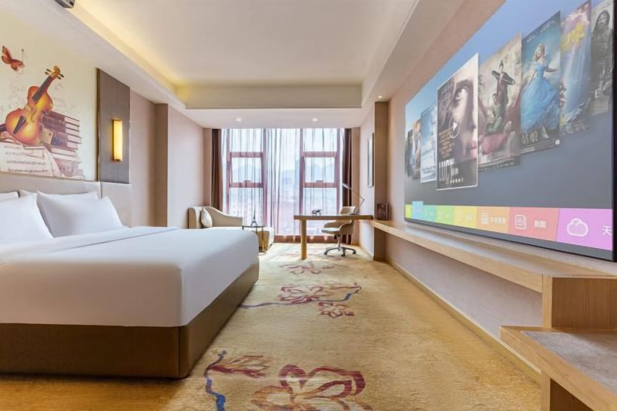 A hotel room with a large bed, a desk, and a TV mounted on the wall displaying movie posters.