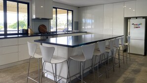 A modern kitchen with a central island, white bar stools, a stainless steel refrigerator, and large windows providing natural light. - 2 minutes to the Murray River large Family home<br> (Bundalong)