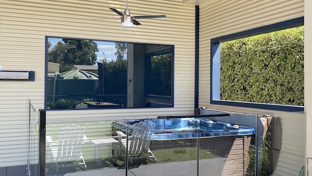A modern outdoor area with a glass-enclosed hot tub, a ceiling fan, and a view of a garden. - 2 minutes to the Murray River large Family home<br> (Bundalong)