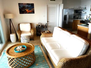 A living room with a sofa, chairs, a coffee table, and a kitchen area with a refrigerator and microwave.