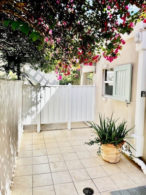 A tiled patio area with a white fence, a potted plant, and a building with a window and shutters. - Just Right Villa St John, Wishing you wonderful memories of St John! (Coral Bay)