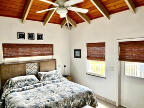 Ein Schlafzimmer mit Bett, Deckenventilator, Holzbalken und zwei Fenstern mit Jalousien.