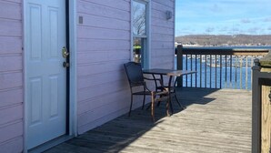 A pink building with a 'STUDIO' sign, a door, and a table with chairs on a wooden deck overlooking a body of water. - Studio D Sleep 6- Bachelor/Bachelorette Parties! (Lake Ozark)