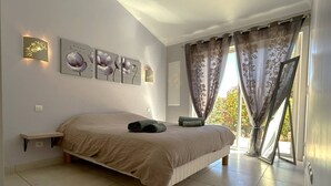 Ein Schlafzimmer mit einem großen Bett, einem Nachttisch, einer Wandleuchte und einem fenster mit Vorhängen.