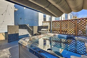 Un bain à remous sur une terrasse en bois, avec une zone couverte au-dessus, un barbecue et une clôture en bois.