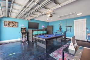 A room with a pool table, dartboards, a bar area, and a neon sign.