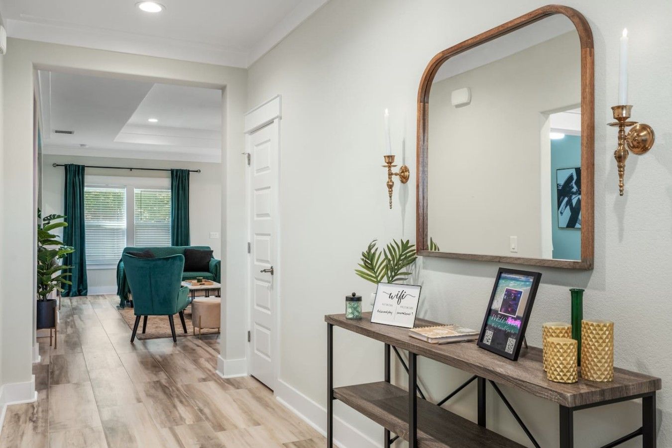 A hallway with a wooden floor, a desk with a mirror, a framed picture, and a potted plant.