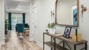A hallway with a wooden floor, a desk with a mirror, a framed picture, and a potted plant. - • Emerald-Gem-Inn • PCB • Family Fun Beach Home! • (Panama City Beach)