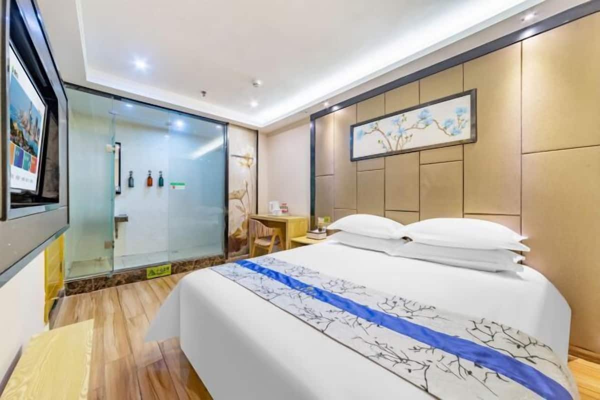 Une chambre d’hôtel comprenant un lit, un bureau, une chaise, une cabine de douche en verre et un tableau au mur.