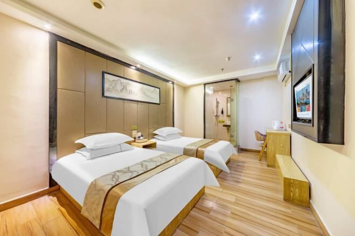 Une chambre d’hôtel avec deux lits, un plancher en bois, un grand téléviseur fixé au mur et un banc.