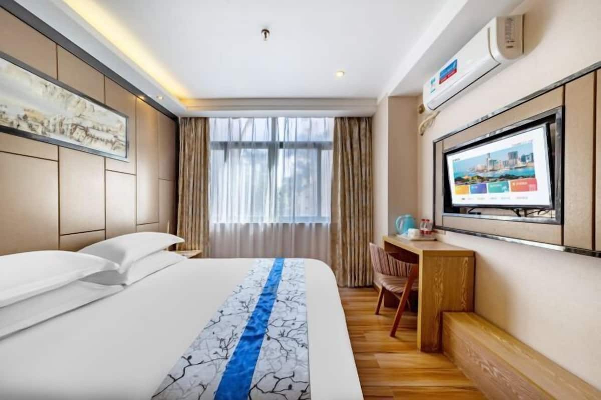 Une chambre d’hôtel avec un grand lit, un bureau, une télévision et une fenêtre avec des rideaux.