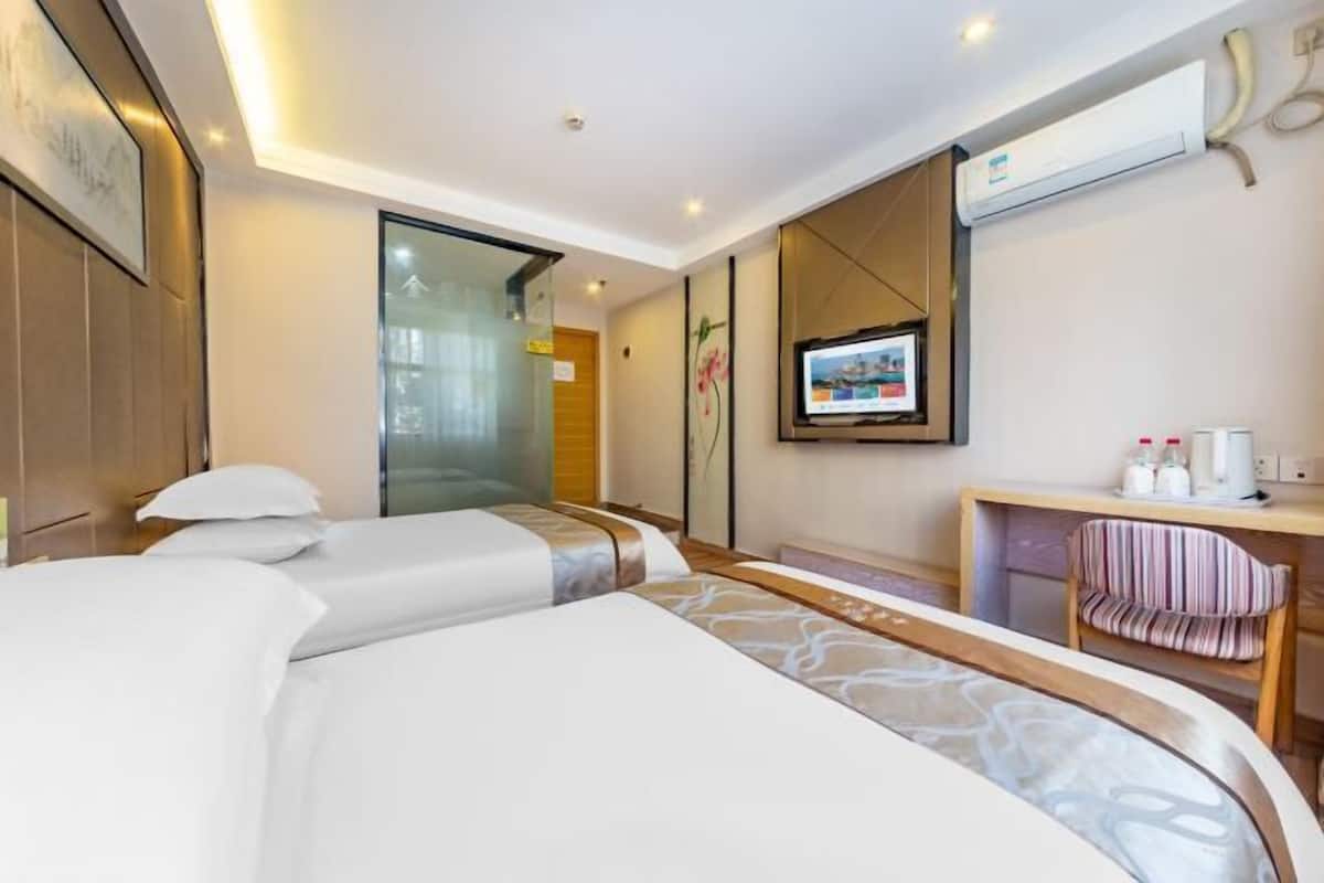 Une chambre d’hôtel avec deux lits, une télévision, un bureau avec une chaise et une grande fenêtre.