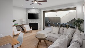 Una sala de estar moderna con chimenea, televisor de pantalla plana, ventilador de techo y comedor con mesa y sillas.