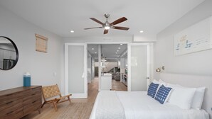 Un dormitorio moderno con una cama grande, un aparador de madera, un ventilador de techo y vistas a la cocina y la sala de estar.