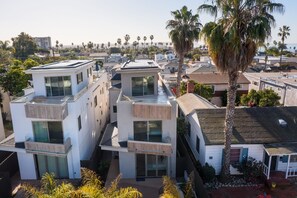A modern residential area with contemporary houses featuring large windows and balconies, surrounded by palm trees and a clear view of the ocean.
