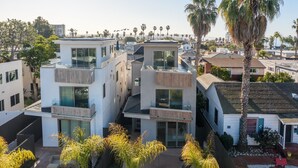 Un edificio residencial moderno de varios pisos con amplios ventanales, balcones y un jardín ajardinado con palmeras.