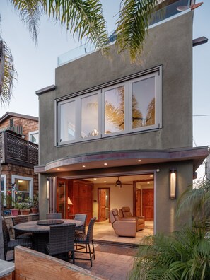 A modern two-story house with a patio area, large windows, and a dining set. - Ocean View Beach Home w/ AC, Outdoor Shower, Walk to PB (San Diego)