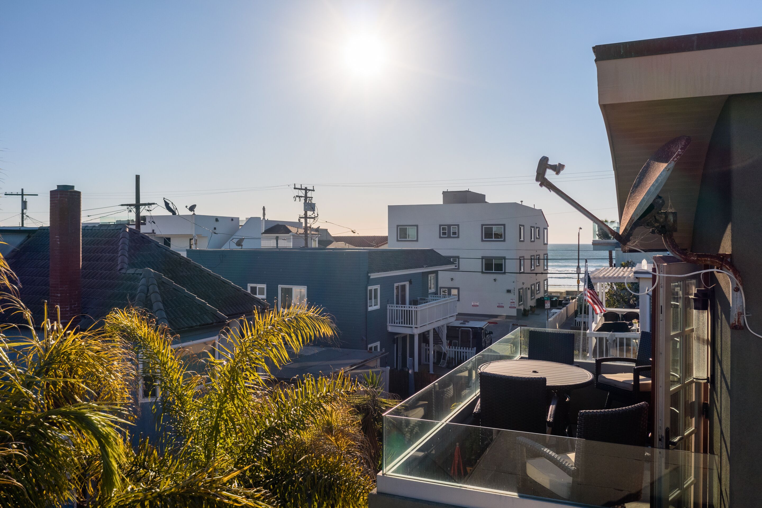 Een balkon met glazen hekwerk met uitzicht op een woonwijk met huizen en een heldere lucht.