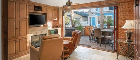 A spacious kitchen with wooden cabinets, a TV, and a grill. There is a seating area with chairs and a table, and a patio with a view of the outside.