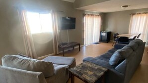 Een ruime woonkamer met een grijze bank, een houten salontafel en een flatscreen televisie aan de muur.