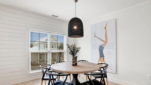 A dining area with a round table, black chairs, a woven pendant light, a vase with flowers, and a large framed artwork on the wall. - 3BR Home @ Summer Salt • Sleeps 9 • Resort Pool & Near Beach (Orange Beach)