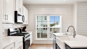A modern kitchen with white cabinetry, a stainless steel stove, and a large window providing a view of the outside. - 3BR Home @ Summer Salt • Sleeps 9 • Resort Pool & Near Beach (Orange Beach)