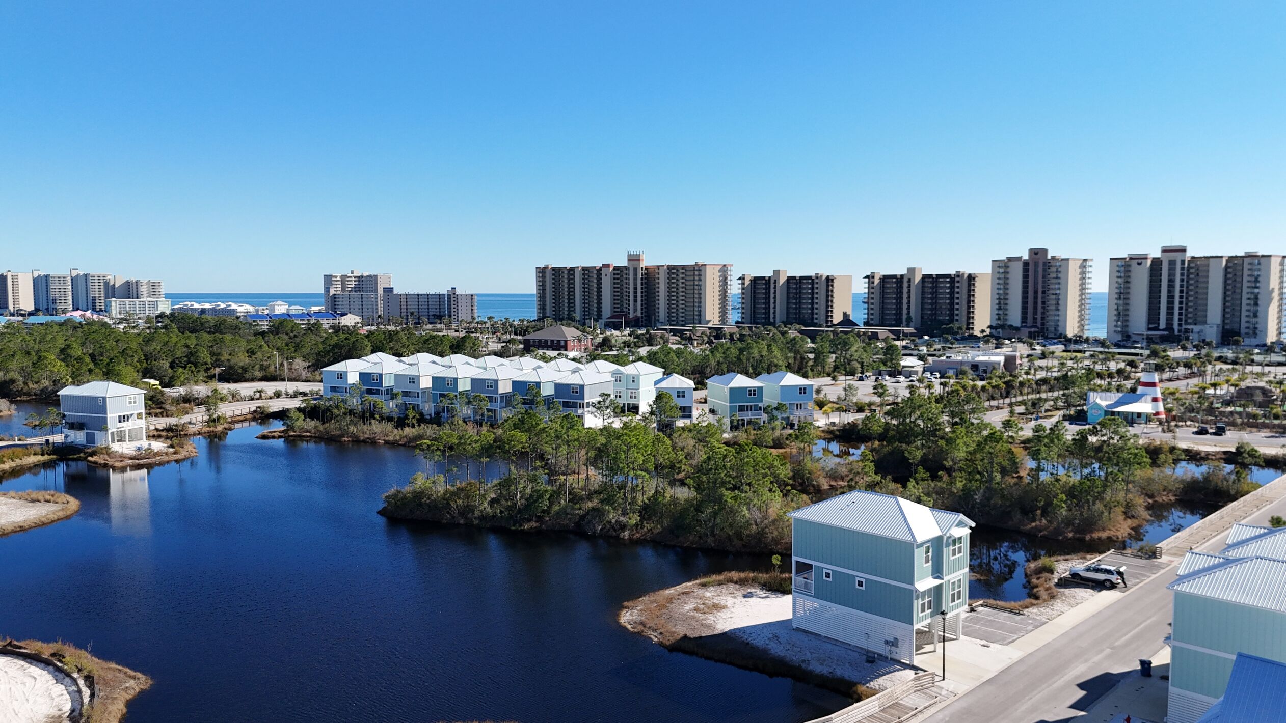 A coastal resort area with multiple beachfront villas, a marina, and high-rise buildings in the background.