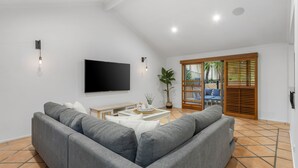 A modern living room with a grey sectional sofa, a flat-screen TV mounted on the wall, a small coffee table with decorative items, and a potted plant.