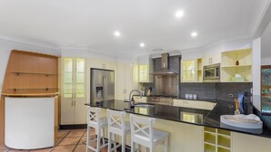 A modern kitchen with a central island, white bar stools, and built-in appliances.