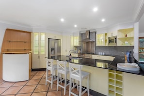 A modern kitchen with a central island, white bar stools, and built-in appliances. - 4BR Family Oasis w/ Pool Modern and Spacious (Robina)